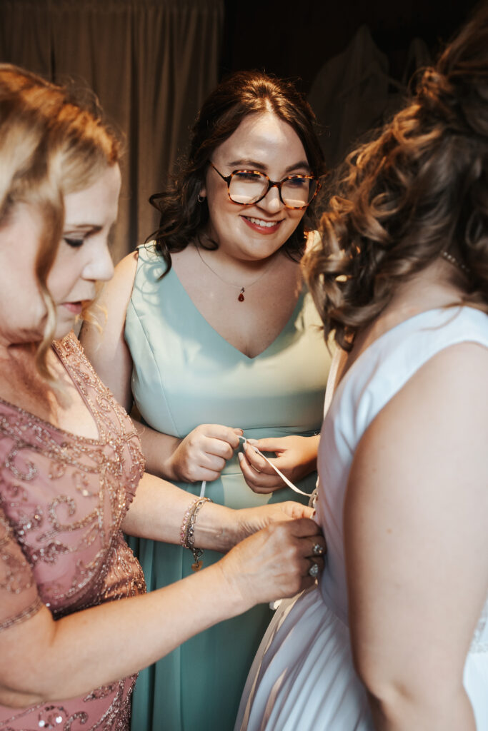 lilly valley press at wedding helping bride into her dress